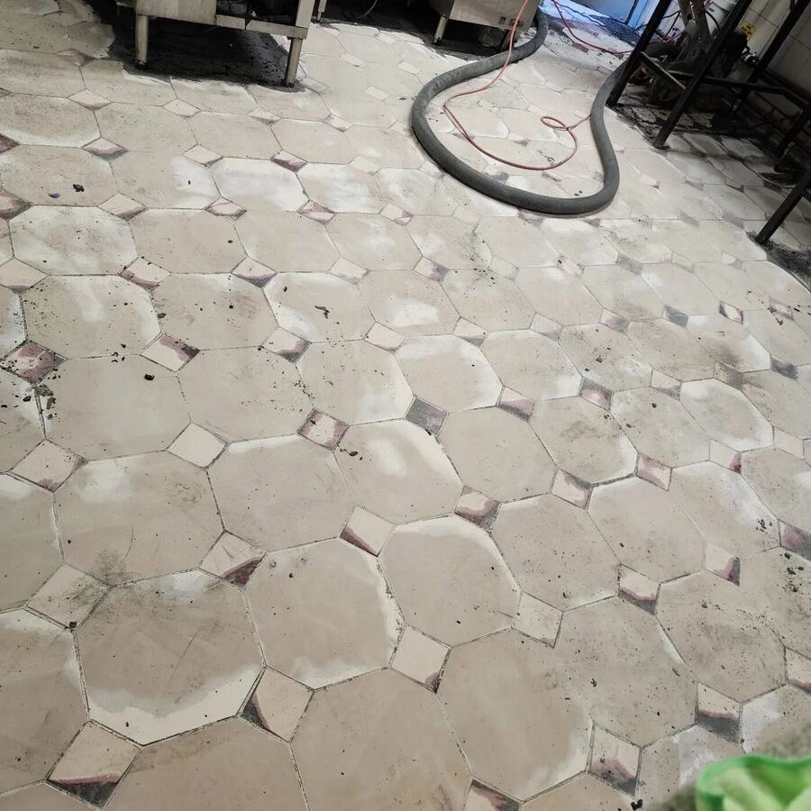 Old tiled commercial floor with a vacuum hose during surface preparation