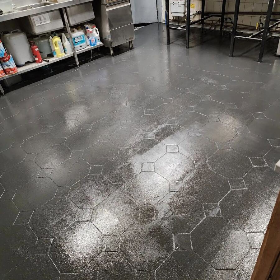 Dark coated floor in a commercial kitchen with shelving of cleaning products