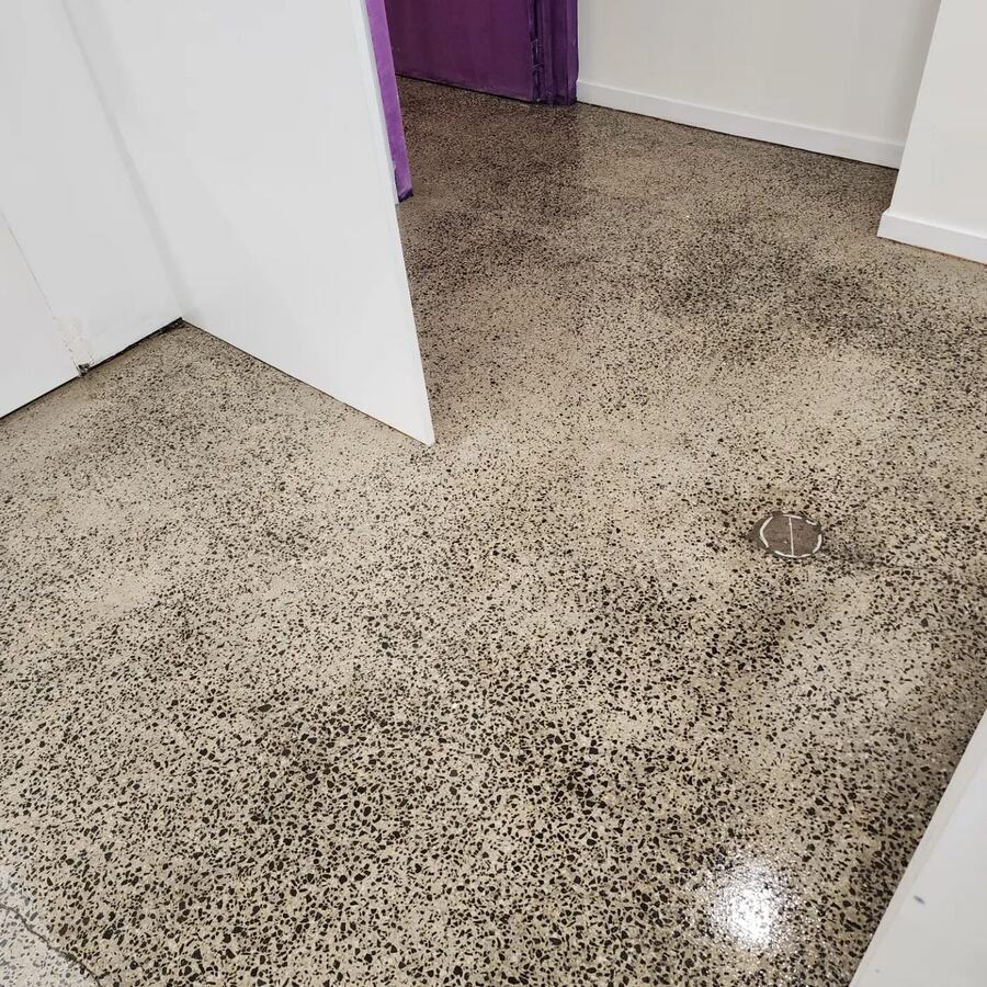 Sealed concrete floor with a patchy matte surface beside white joinery in a commercial space