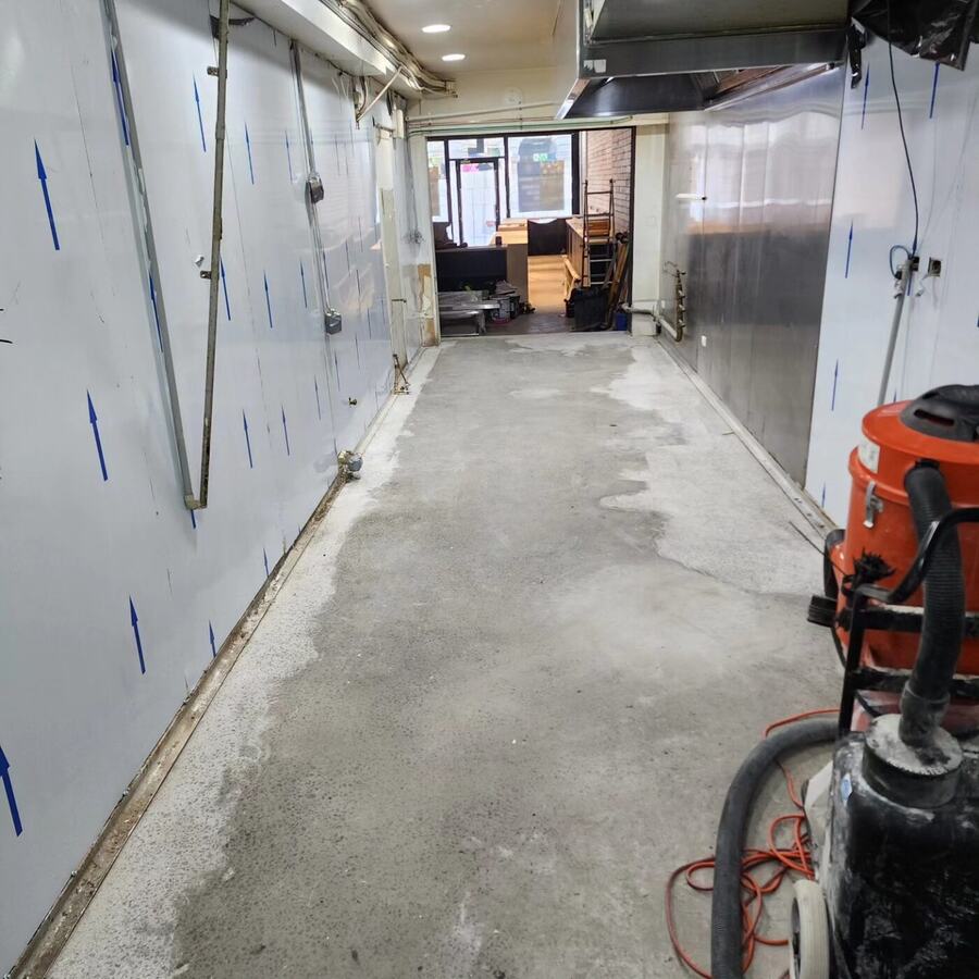 Concrete corridor floor mid-preparation with a dust extractor beside it