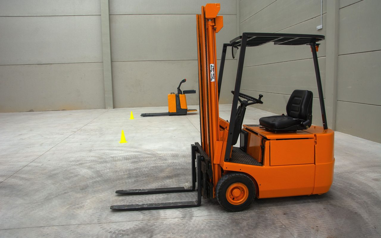 Orange forklift parked on a bare concrete warehouse floor with two traffic cones