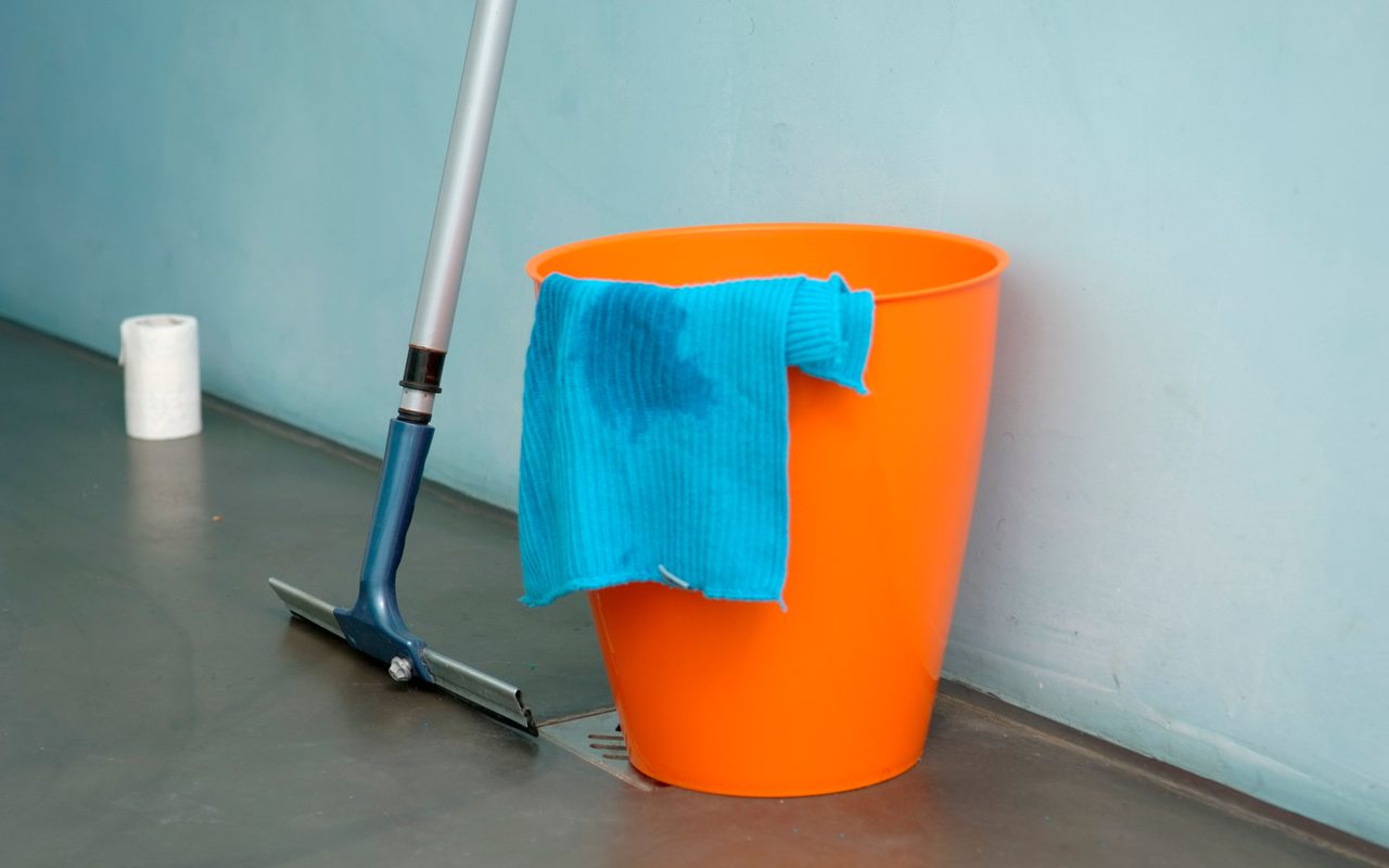 Orange bucket and floor squeegee leaning against a wall on a smooth floor