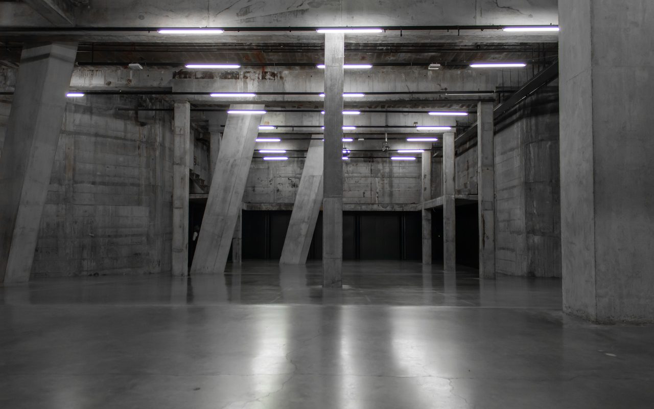 Large empty concrete hall with a smooth reflective floor under fluorescent lights