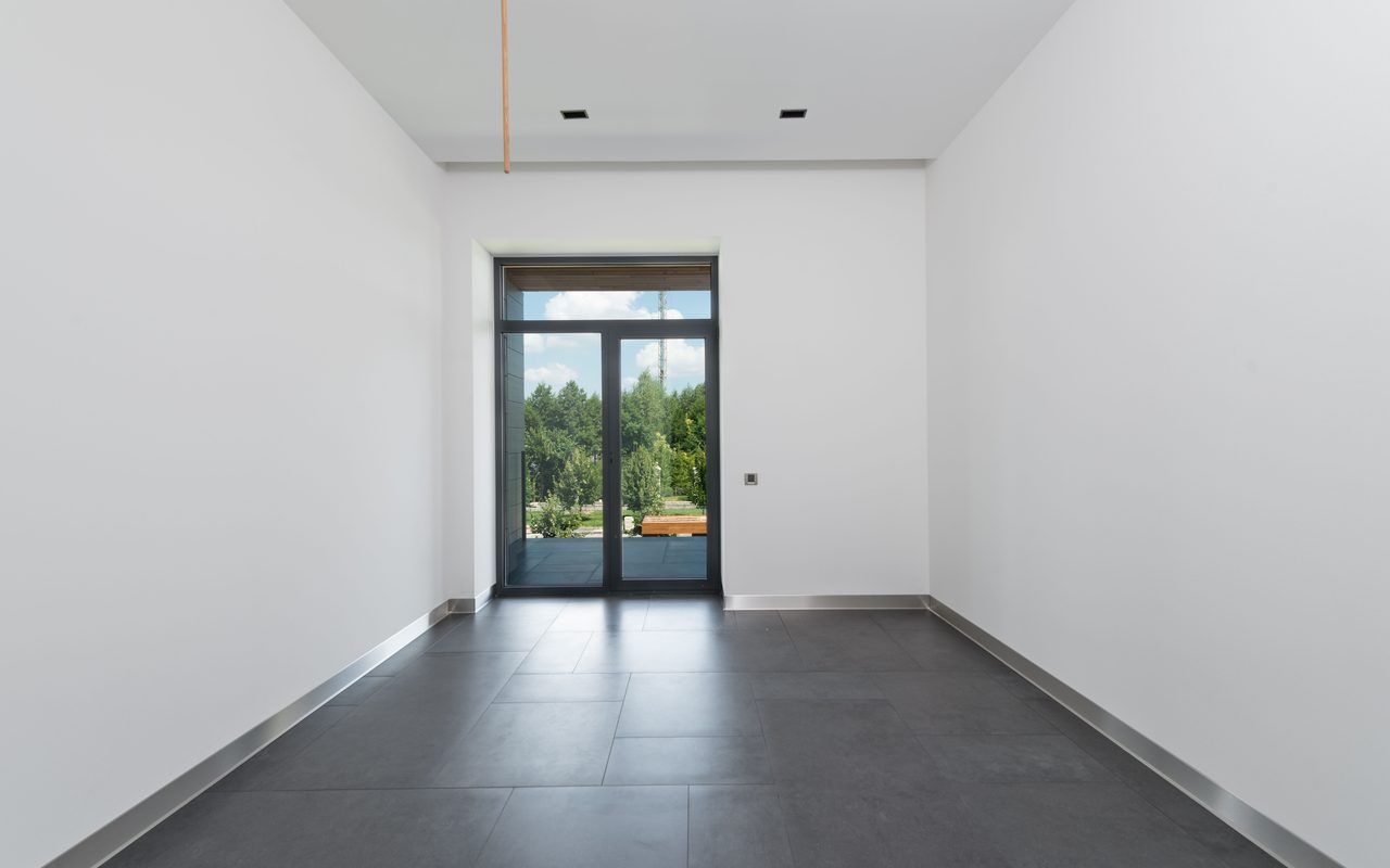 Empty room with a dark tiled floor, white walls and glass doors, shown as a showroom shell