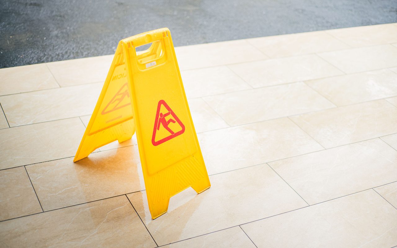 Yellow wet floor caution sign standing on a tiled floor